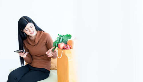 Young woman using phone while standing against wall