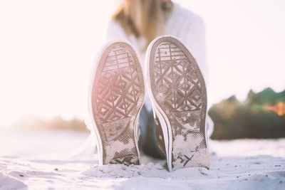 Low section of woman wearing shoes and sitting on beach