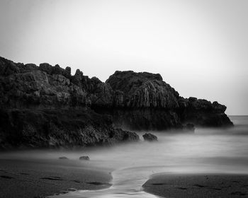 Scenic view of rocks by sea against clear sky