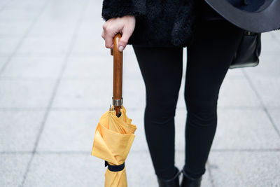 Close-up of a girl's hand holding a yellow closed umbrella.