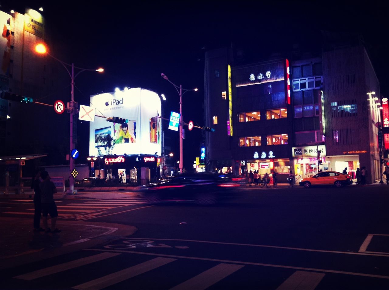 building exterior, night, city, architecture, street, built structure, illuminated, text, city life, road, communication, western script, transportation, city street, men, walking, sign, road marking, road sign