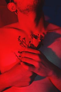 Midsection of man holding rose in red light