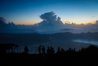 Silhouette people enjoying on hill against cloudy sky during sunset