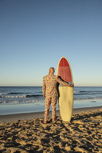 Man in suit holding surfboard while standing at beach