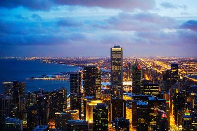 High angle view of illuminated city buildings against cloudy sky