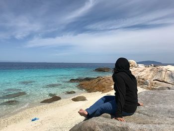 Man sitting on shore at beach against sky