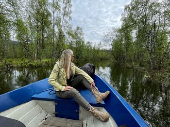 Woman sitting on boat in lake against trees