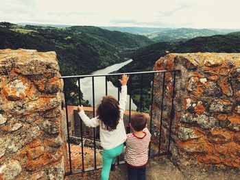 Siblings climbing on gate against mountains