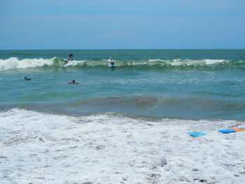 People surfboarding in sea against sky