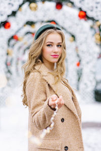 A cute young woman holds in her hand the lights of a garland on the background of a christmas market