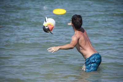 Shirtless man throwing plastic disc while standing in sea