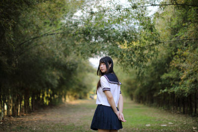 Portrait of young woman standing on field in forest