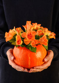 Close-up of hand holding orange rose flower against black background