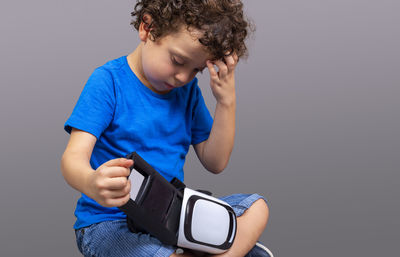 Little boy with virtual reality goggles in his hands looking curiously at how they work