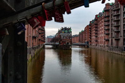 Canal by buildings in city against sky