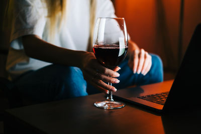 Midsection of man holding wine glass while sitting on table