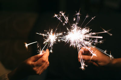 Cropped image of hands holding sparklers at night