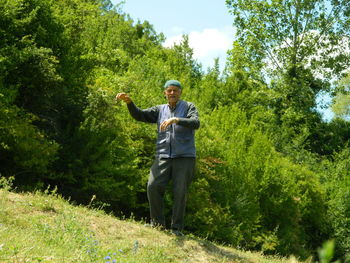 Low angle portrait of man dancing on grassy field against trees