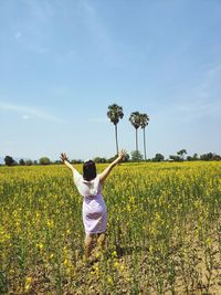 Rear view of person standing by yellow flowers on field