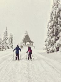 Rear view of people skiing on snow covered field against sky