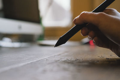 Close-up of human hand holding pencil on table