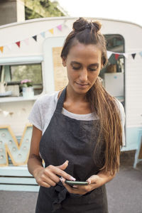 Female owner using smart phone on street against food truck