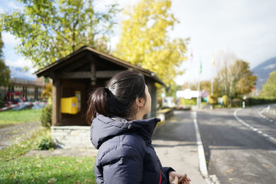 Side view of young woman standing on road during sunny day