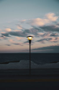 Street light by sea against sky during sunset