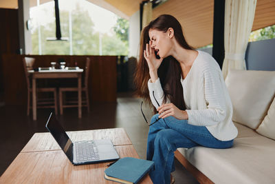 Young woman using mobile phone while sitting on sofa at home