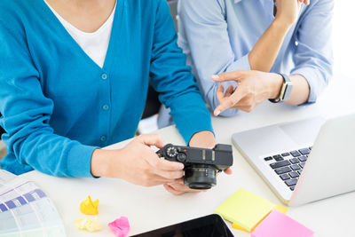 Midsection of woman with man holding camera at table