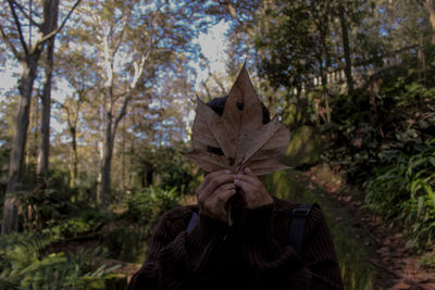 Person with face covered by leaf standing at forest