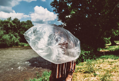 Man wearing plastic bag while standing against lake