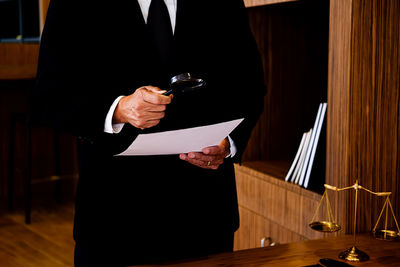 Midsection of lawyer holding magnifying glass over paper