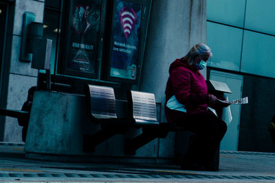 Side view of woman using mobile phone while standing against wall