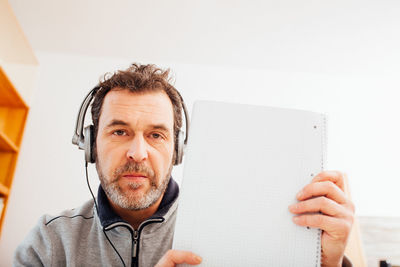 Mature adult male teacher showing note pad into camera in home schooling chat 