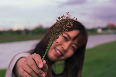 Portrait of young woman holding plant on field