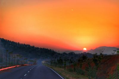 Road by trees against orange sky