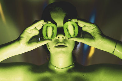 Young woman covering eyes with kiwi fruits