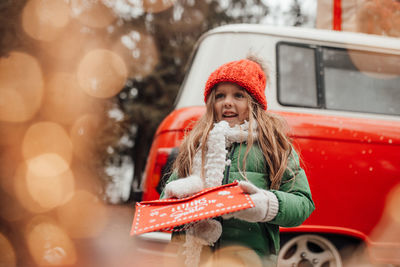 Cute smiling girl standing against car during winter