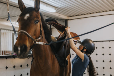 Woman in stable putting saddle on horse