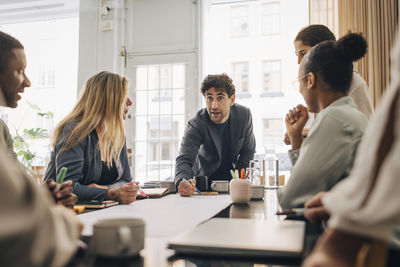 Young entrepreneur explaining business strategy to male and female coworkers in meeting room at office