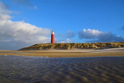 Lighthouse on beach by sea against sky