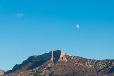 Low angle view of rock formation against clear blue sky with moon