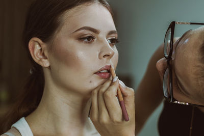 A young makeup artist paints a girl s lips with a pencil.