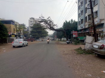Cars on street by buildings in city against sky