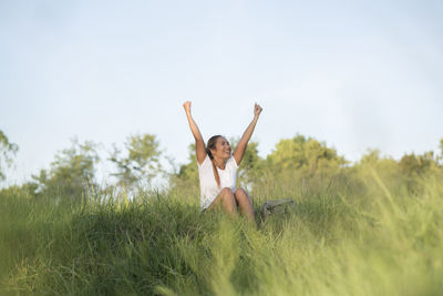 Smiling woman clenching fists while sitting on field against sky