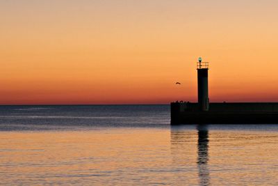 Lighthouse by sea against sky during sunset