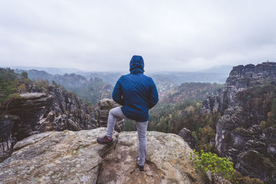 Rear view of man standing on rock looking at mountain against sky