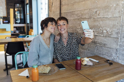 Young friends smiling while taking selfie through mobile phone sitting at restaurant