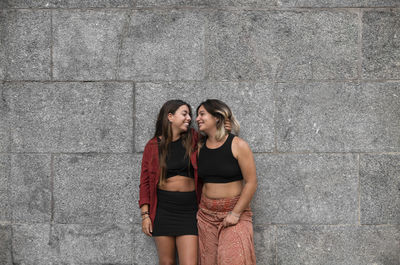 Portrait of two girls standing against stone wall